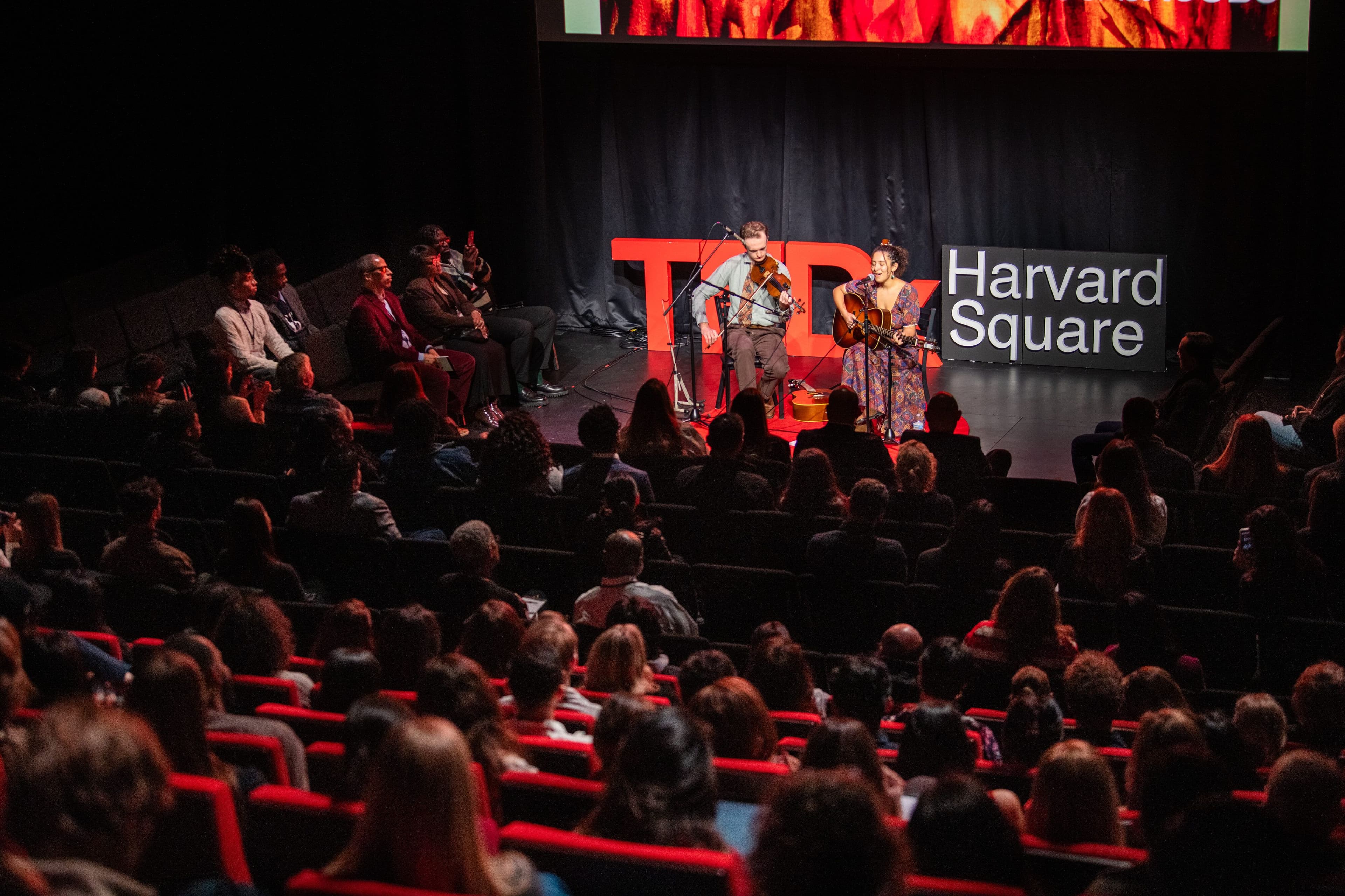 A violinist and a guitarist perform on the TEDx stage in front of a full house.